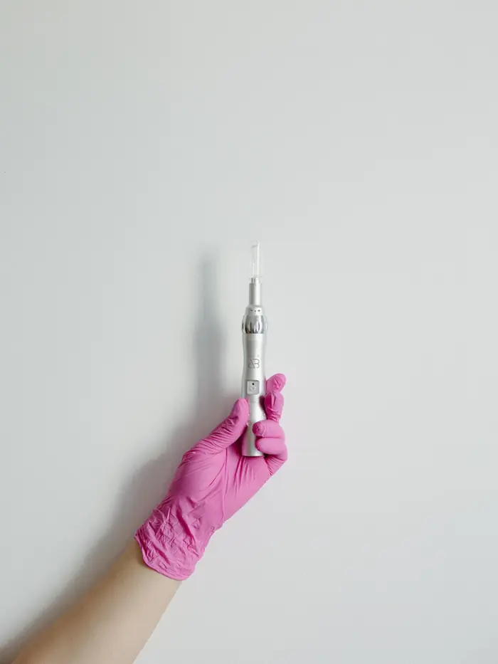 Gloved hand holding a microneedling pen