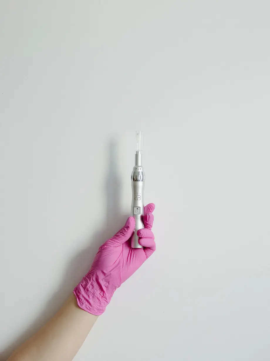 Gloved hand holding a microneedling pen
