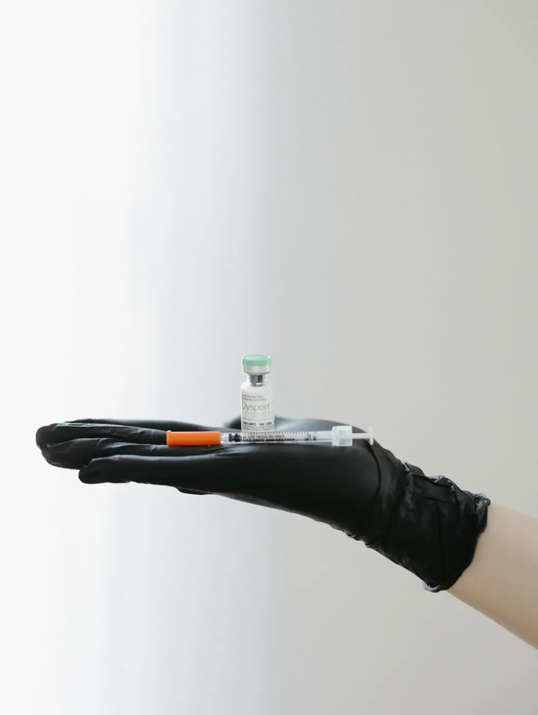 Gloved hand holding a syringe on a pale background