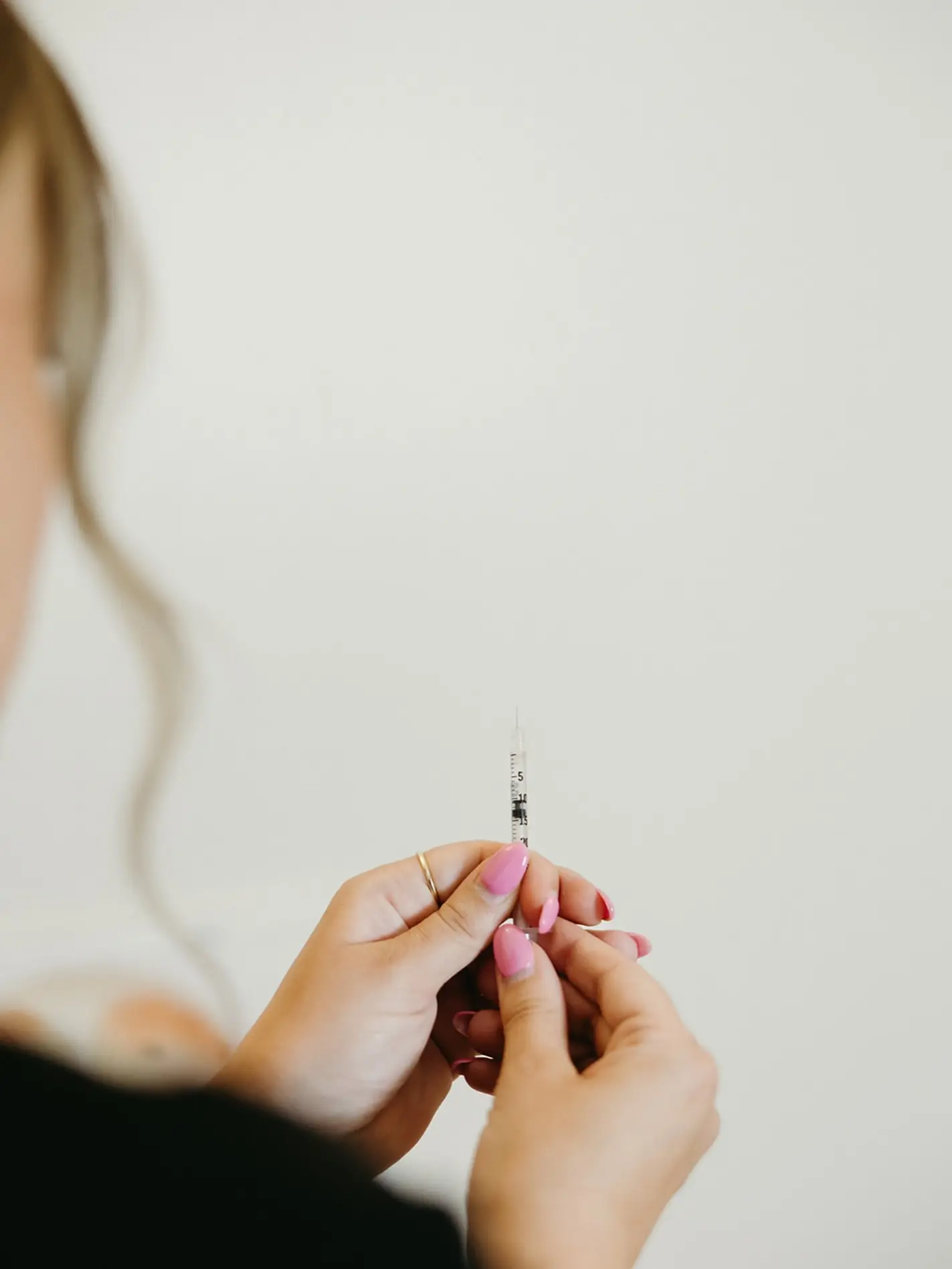Hand holding a syringe against a pale wall
